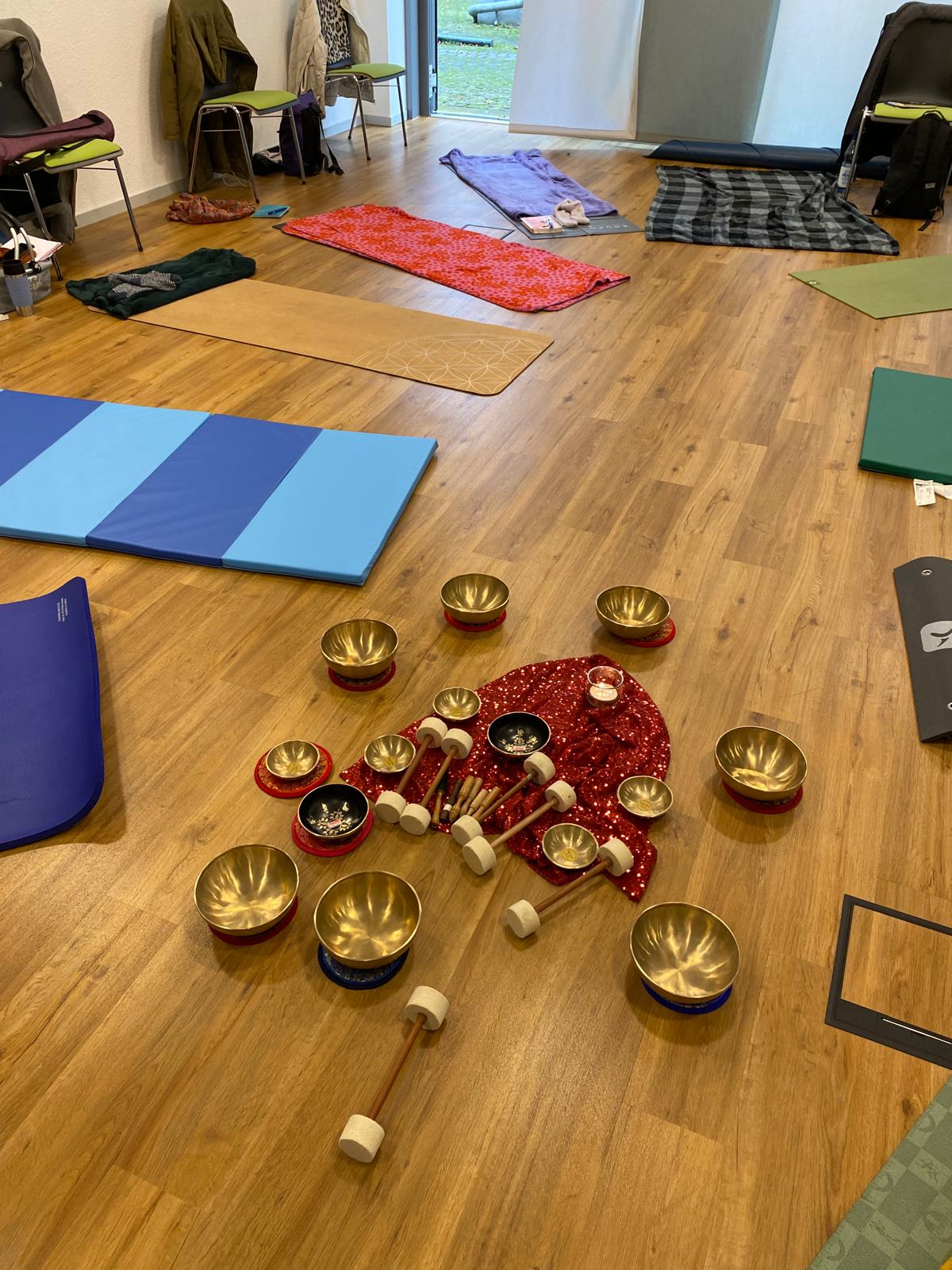 Ein Raum mit Matten im Kreis ausgelegt in der Mitte auf einem roten Tuch stehen viele Klangschalen mehr t Schlegel